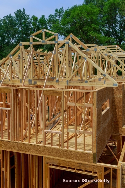 Wood framing of a new suburban home under construction, showing roof trusses and structural beams. Example suburban housing supply crisis